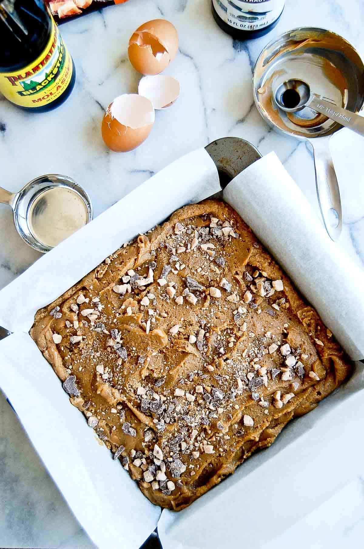 batter for peanut butter blondies in pan on cutting board with cooking tools around the pan.