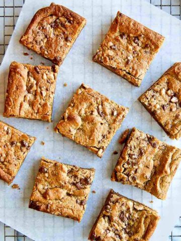 peanut butter blondies on parchment paper and cooling rack, cut into squares.