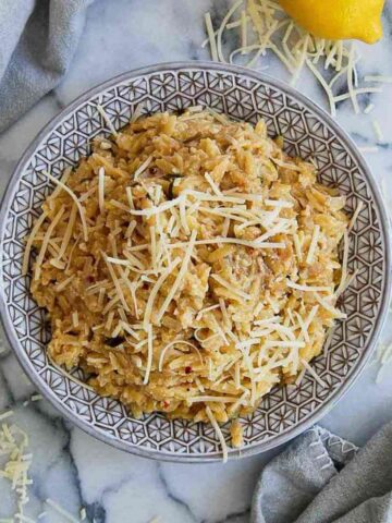 creamy orzo with brown butter in bowl on serving board with parmesan and lemon sprinkled around it.