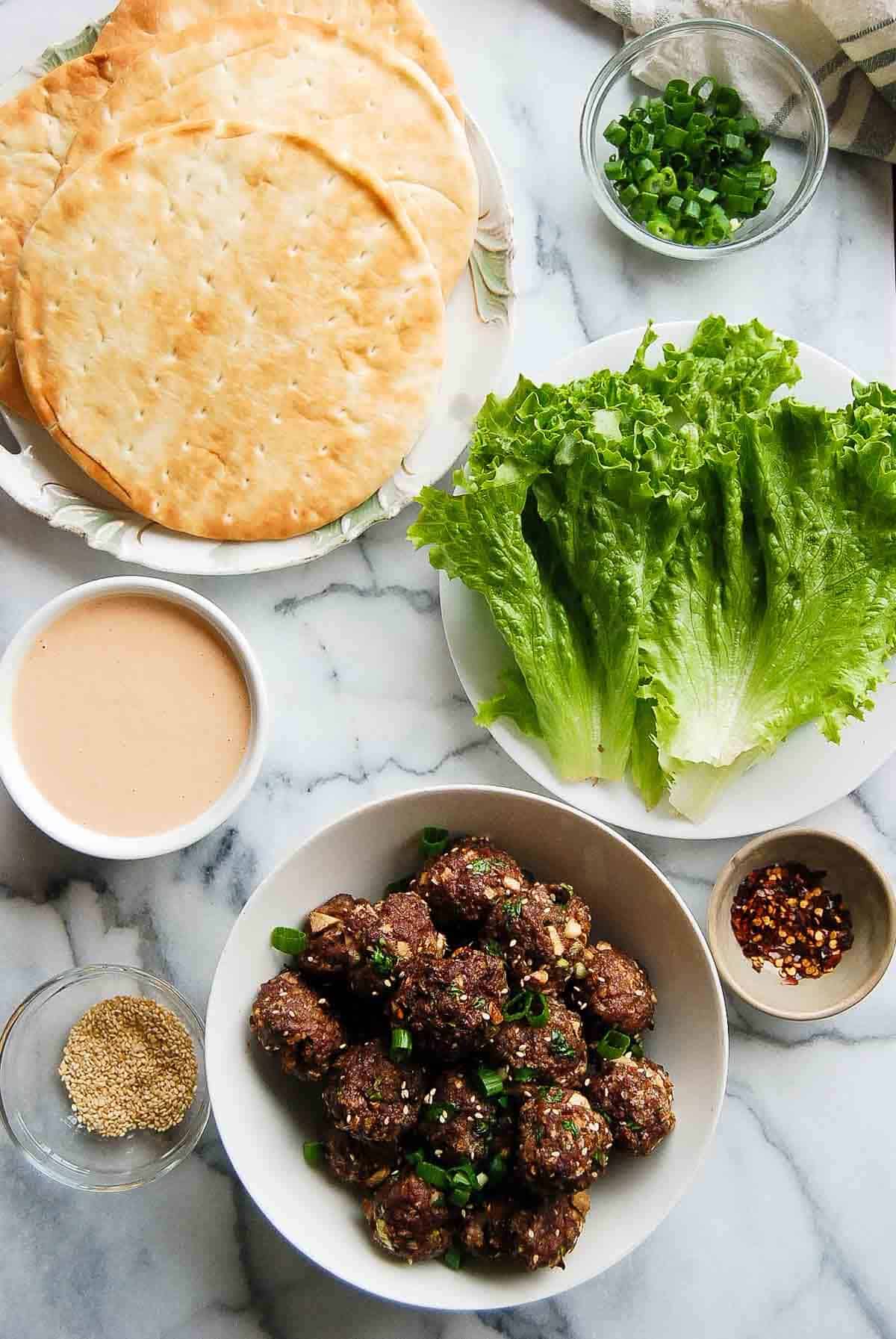 firecracker meatballs in bowl with pita bread, lettuce, spicy sauce and garnishes.