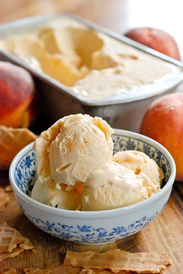 sweet peach ice cream in bowl with waffle cones scattered and pan of ice cream in the background. 