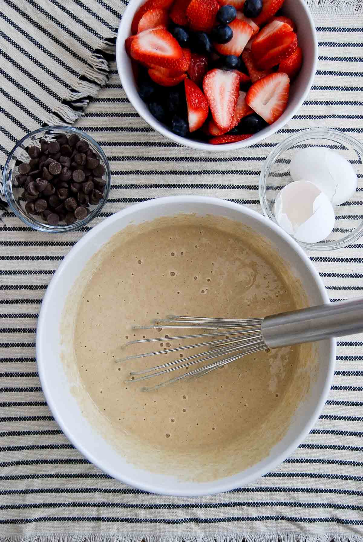 pancake mix in bowl with bowls of strawberries and blueberries, and chocolate chips to the side.