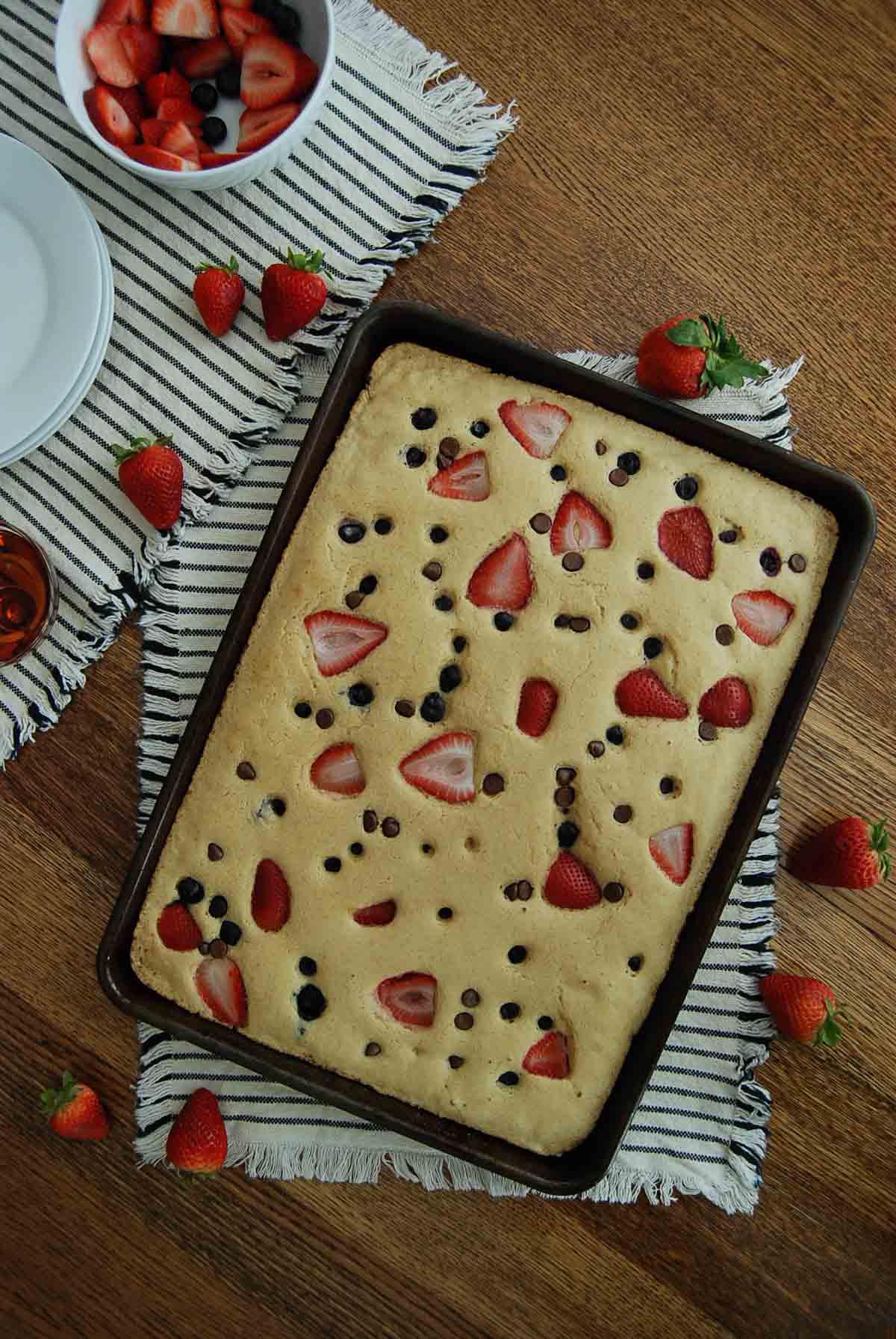 sheet pan pancakes made from mix in pan with strawberries, blueberries and chocolate chips.