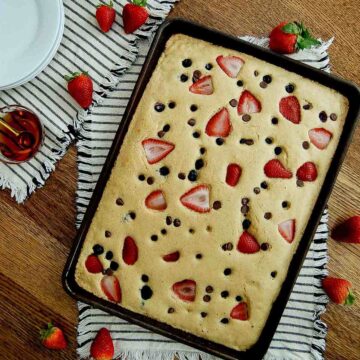 sheet pan pancakes with mix in pan with strawberries, blueberries and chocolate chips.