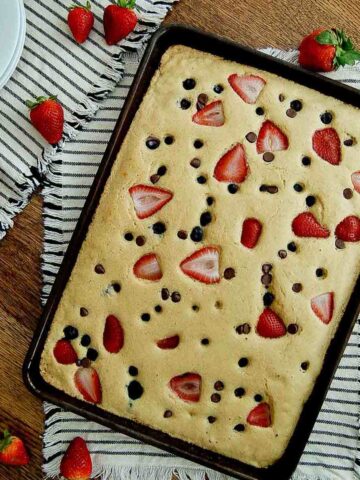 sheet pan pancakes with mix in pan with strawberries, blueberries and chocolate chips.