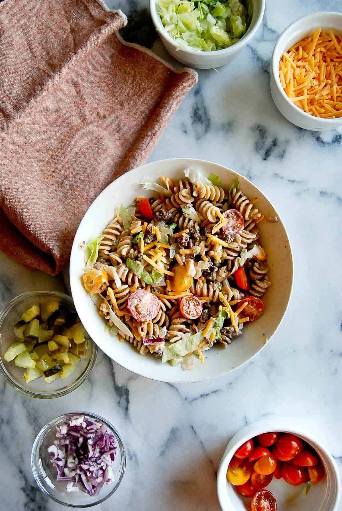 Jimmy Buffett Cheeseburger pasta salad in bowl with ingredients scattered around.