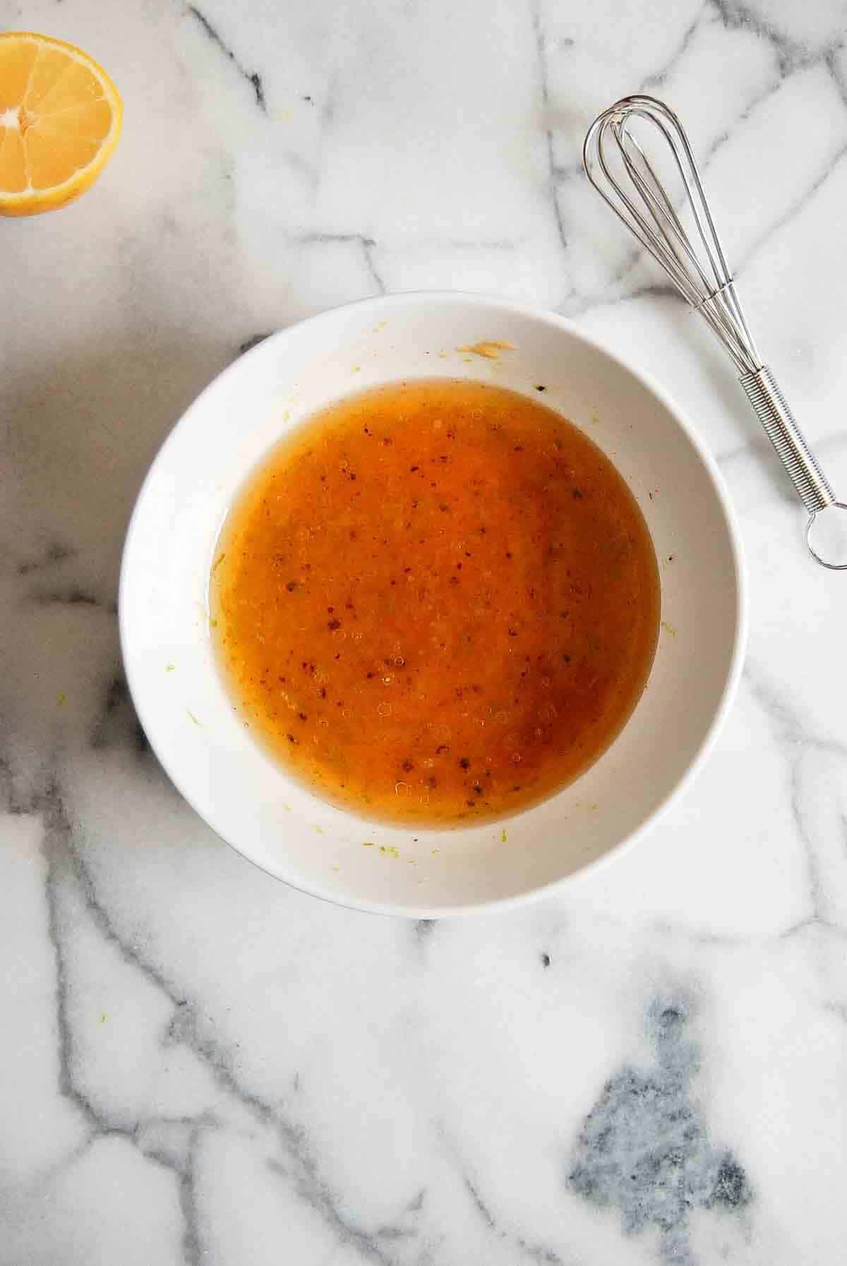 honey dijon dressing in bowl with whisk and lemon to the side.