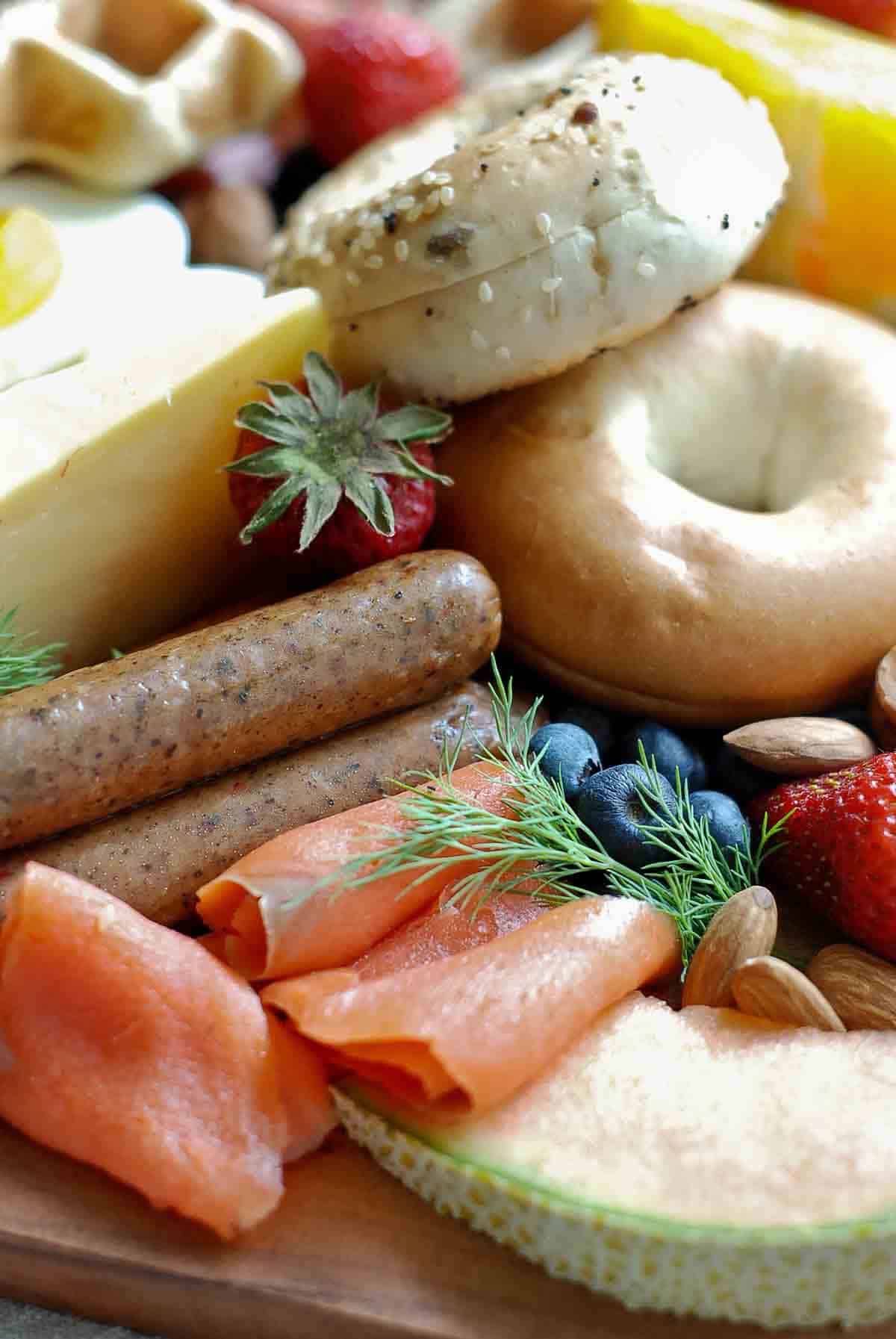 closeup of smoked salmon, sausages, cheese, fruit and bagels.