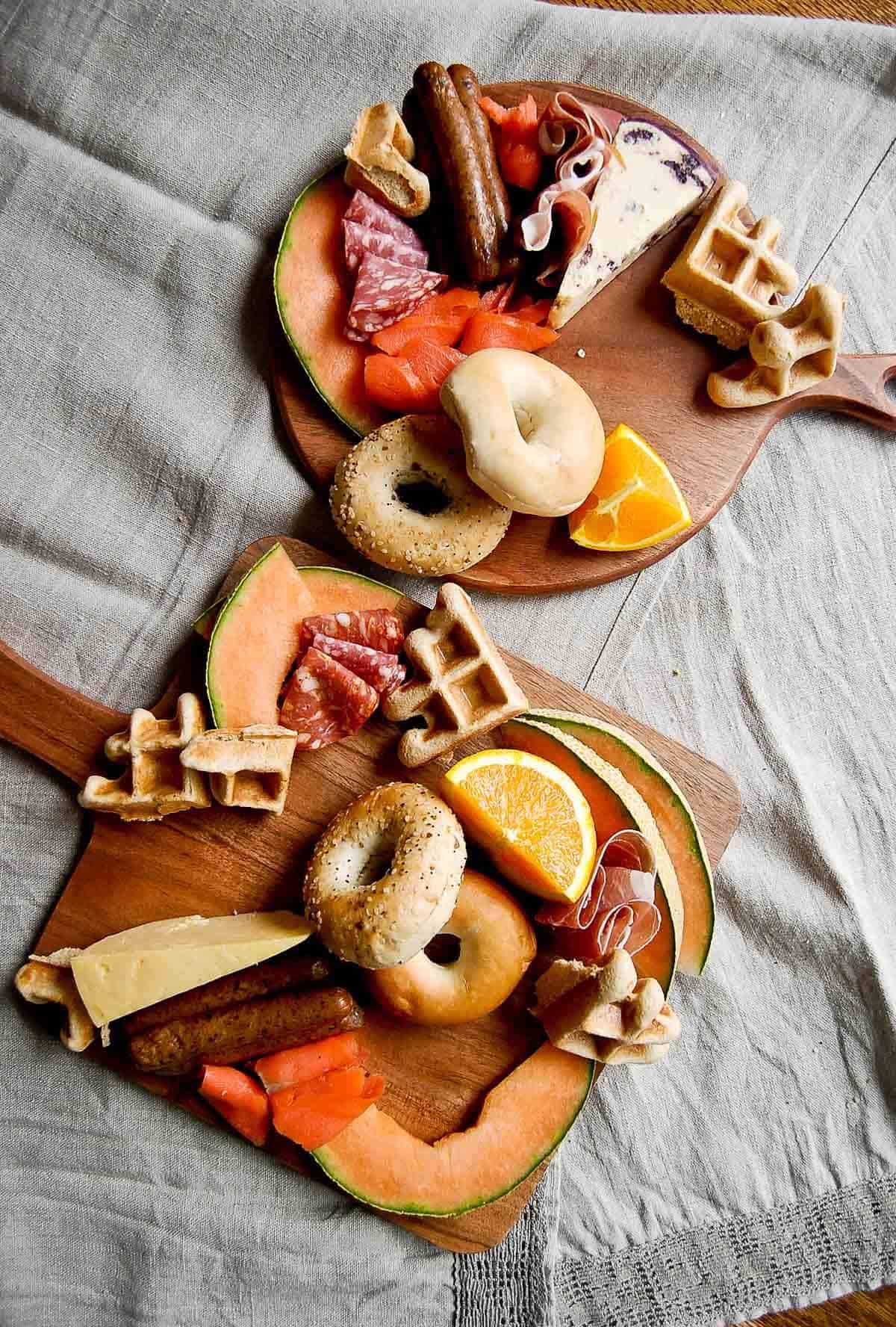 breakfast board with cheese, meats, fruit, salmon, bagels and waffles.