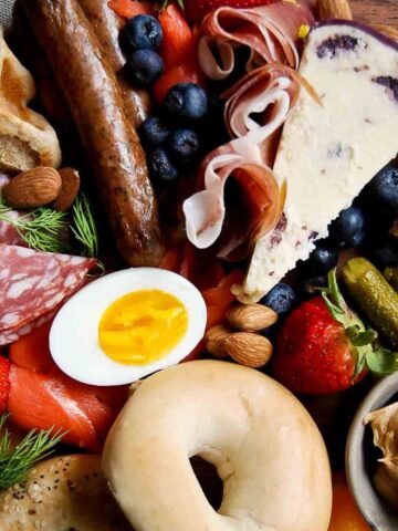breakfast charcuterie board with fruit, bagels, waffles, cheese, meats, spreads, and egg.