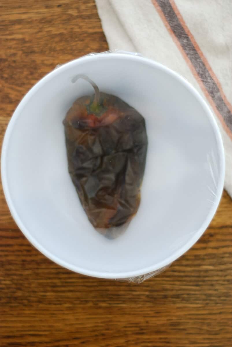 roasted pasilla pepper in bowl covered with plastic.