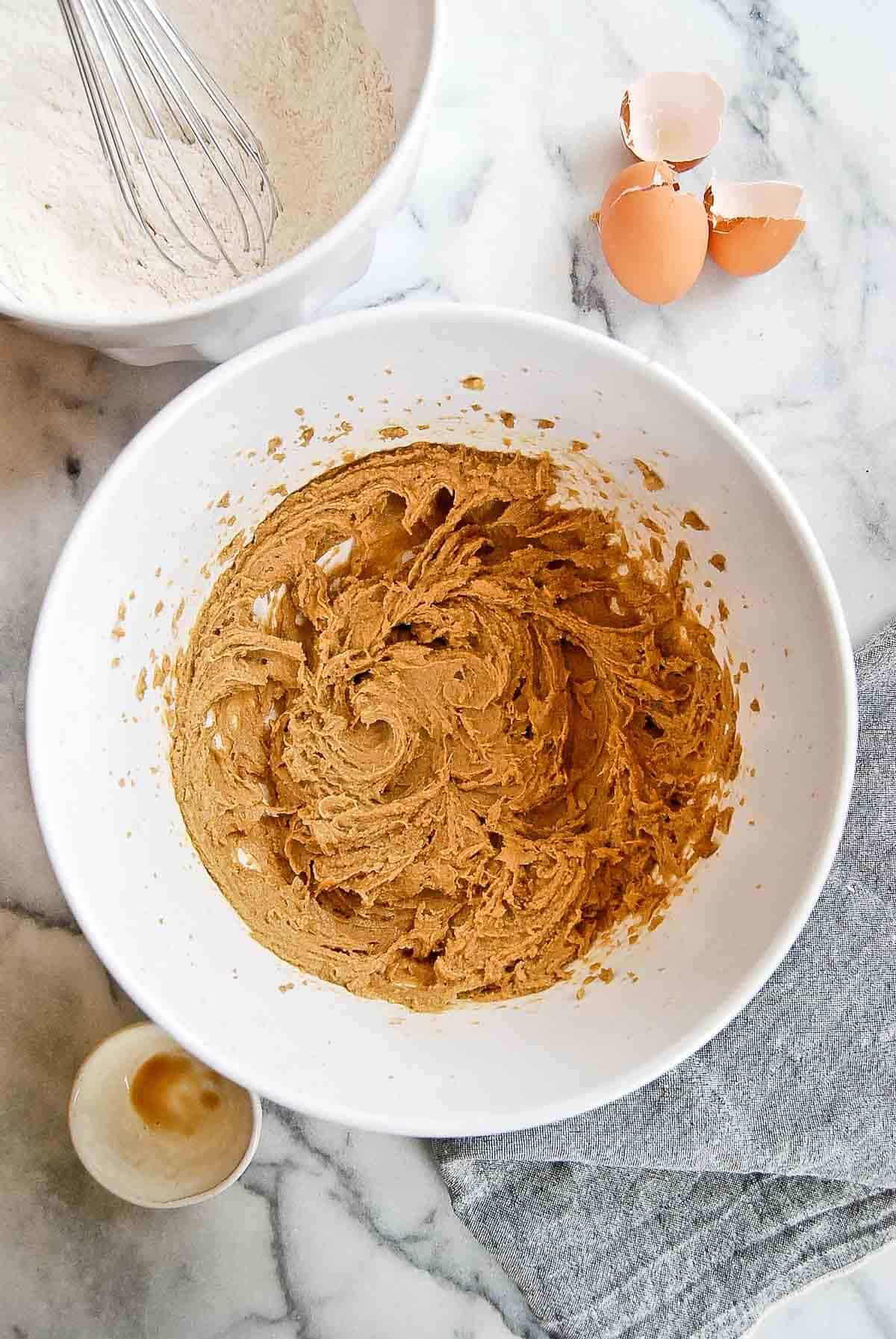 egg, butter and sugars mixed in bowl with egg shells to the side.