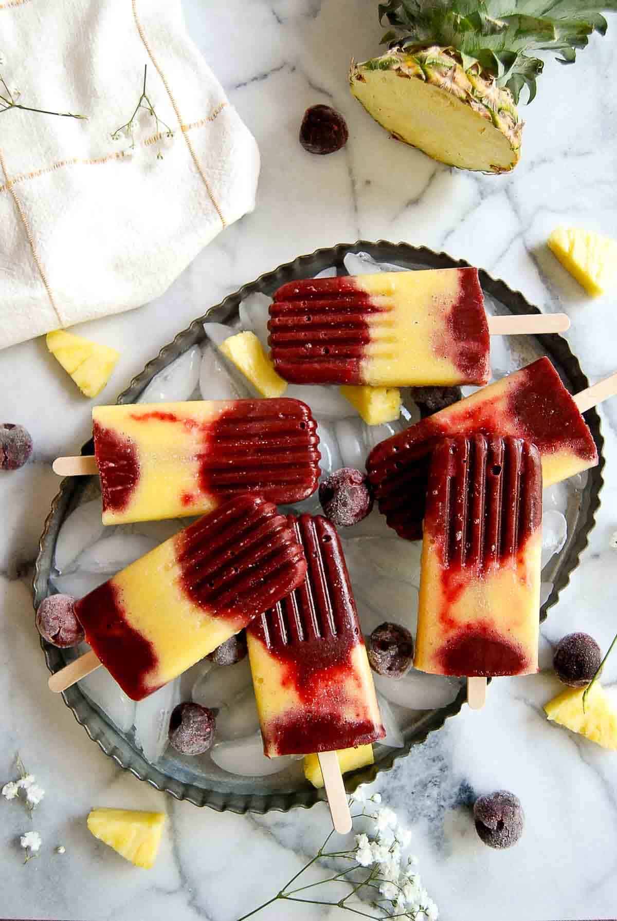 tray of cherry pineapple popsicles on tray with ice.