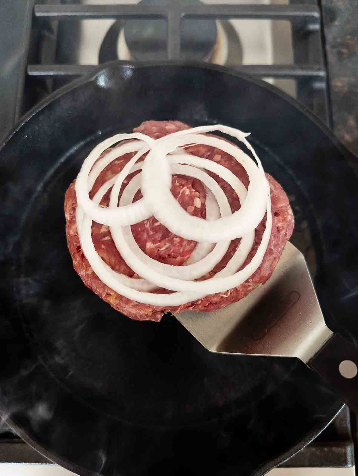 smash burger in skillet with onion on top.