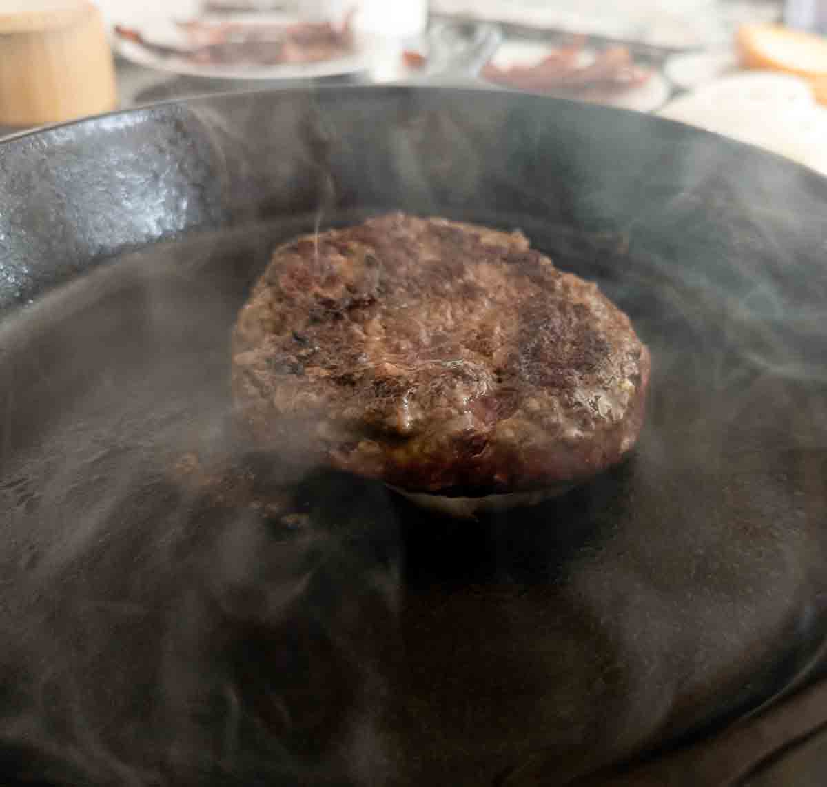 side view of smash burger cooking in skillet.