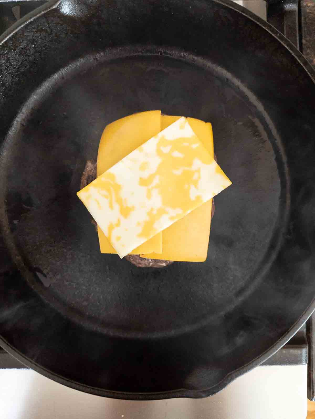 smash burger cooking in skillet with cheese slices on top.