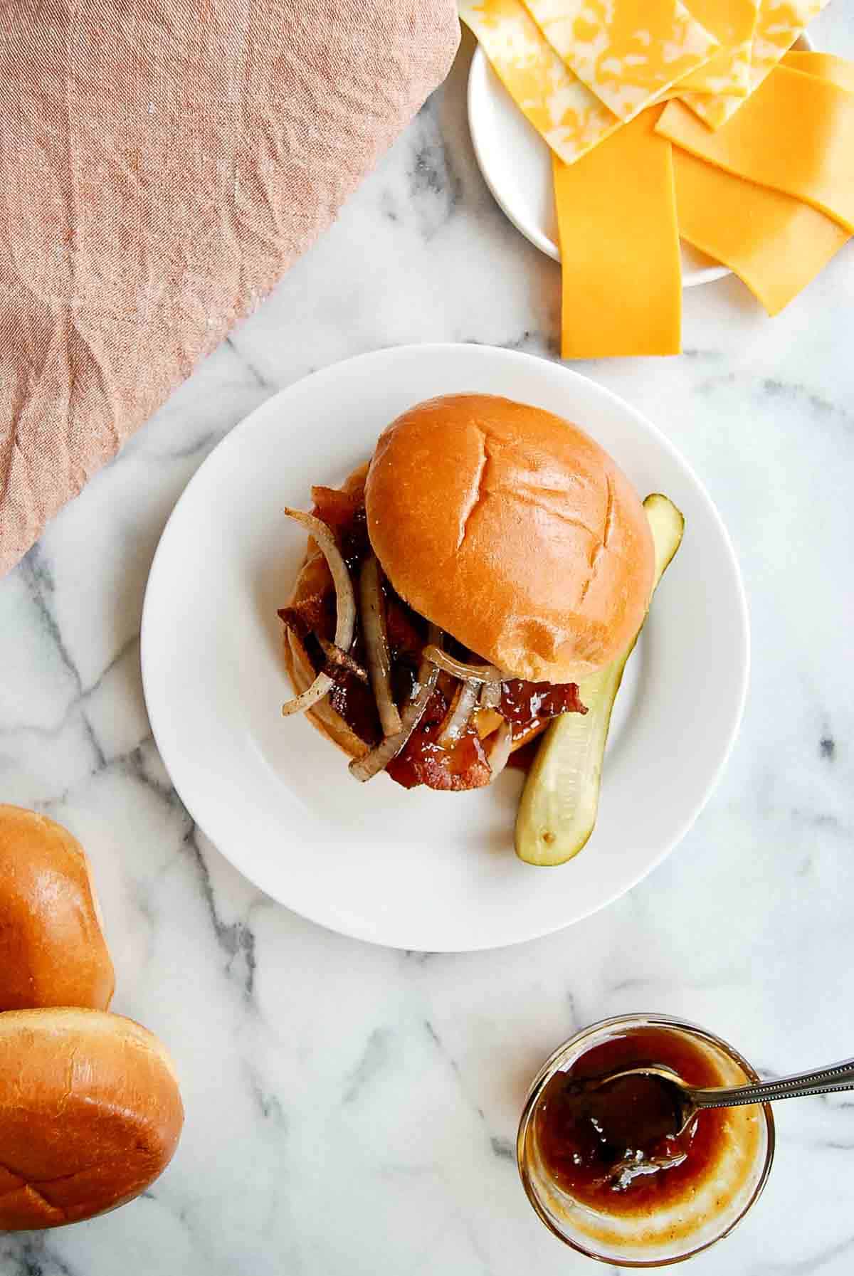 Top down view of sweet and spicy burger on plate with buns, extra cheese and sauce around it.