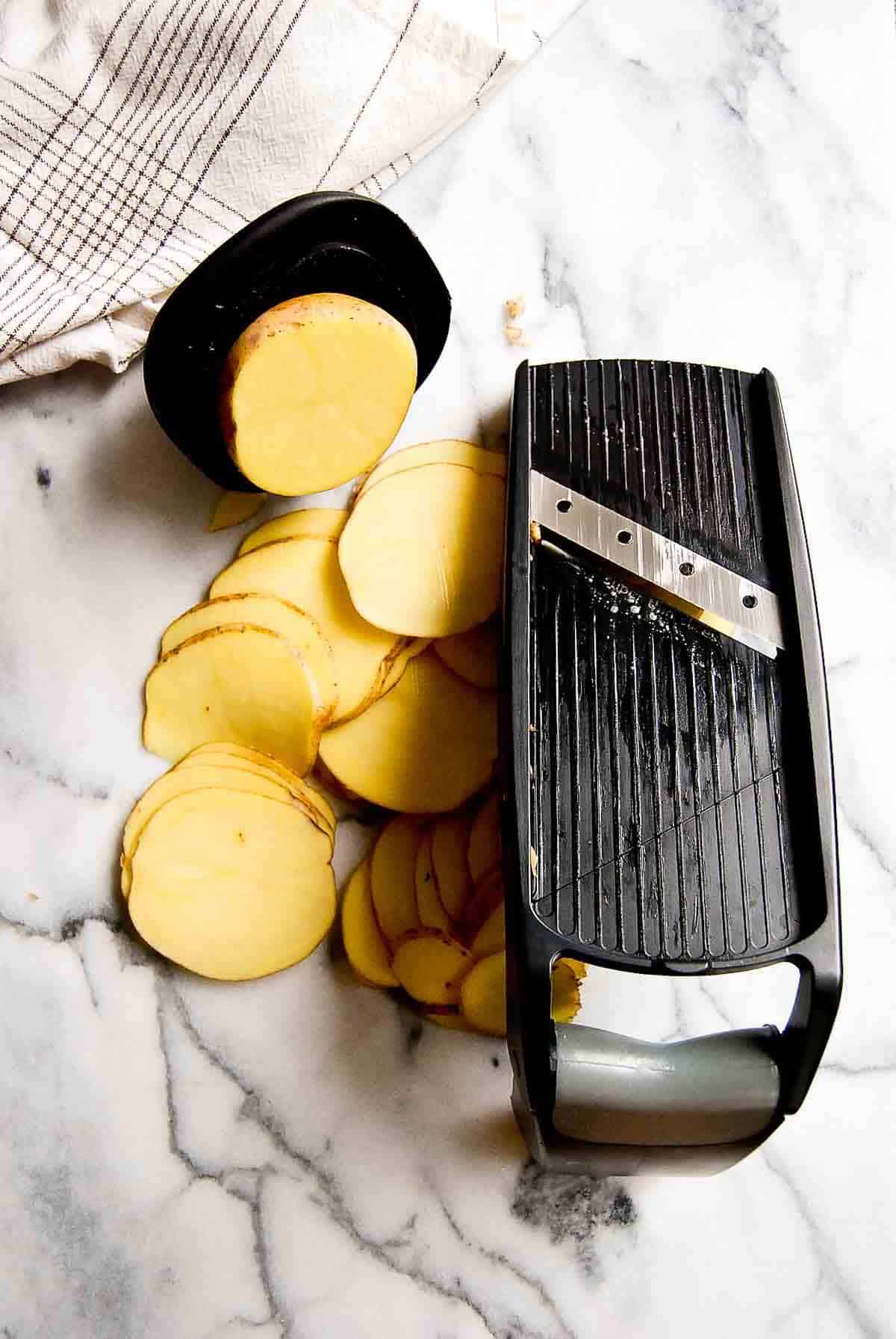 a mandolin with slices of yukon gold potatoes on a cutting board.