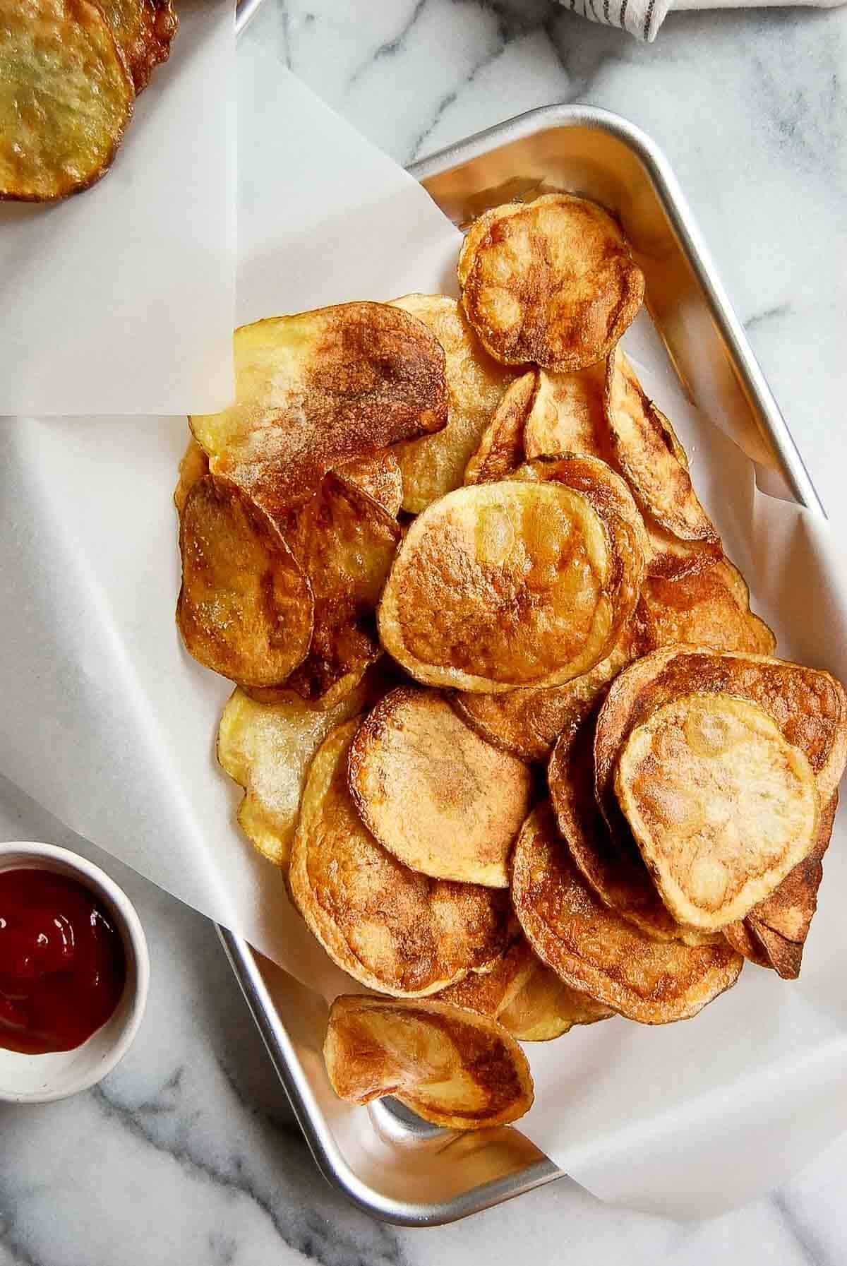 tray with a stack of homemade yukon gold potato chips and a side of ketchup.