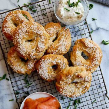 Salt bagels on cooling rack with smoked salmon and cream cheese on the side.