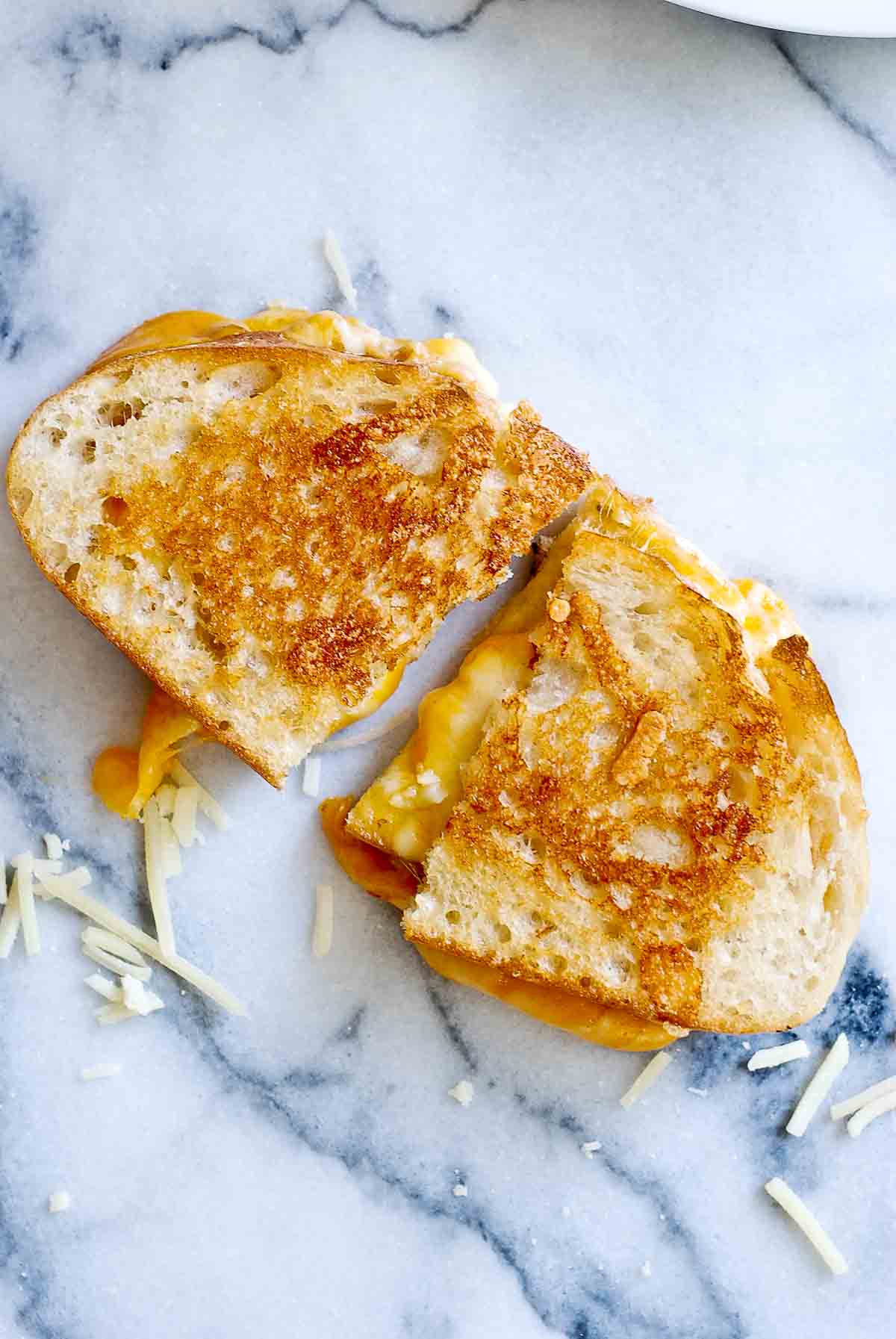 sourdough grilled cheese sandwich cut in half on marble cutting board.