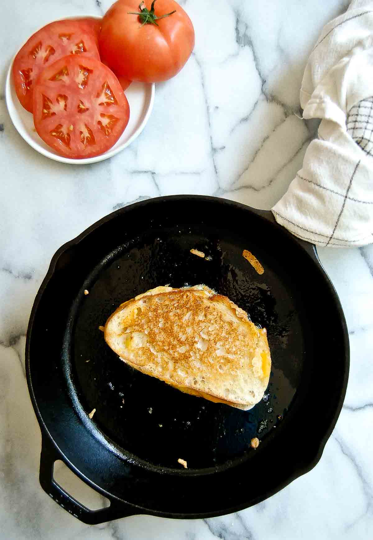 crispy sourdough grilled cheese in cast iron skillet with plate of tomatoes to the side.