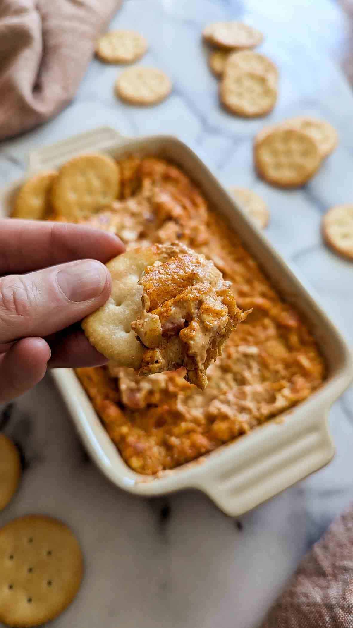 closeup of someone holding ritz cracker with hot cajun crab dip on it.