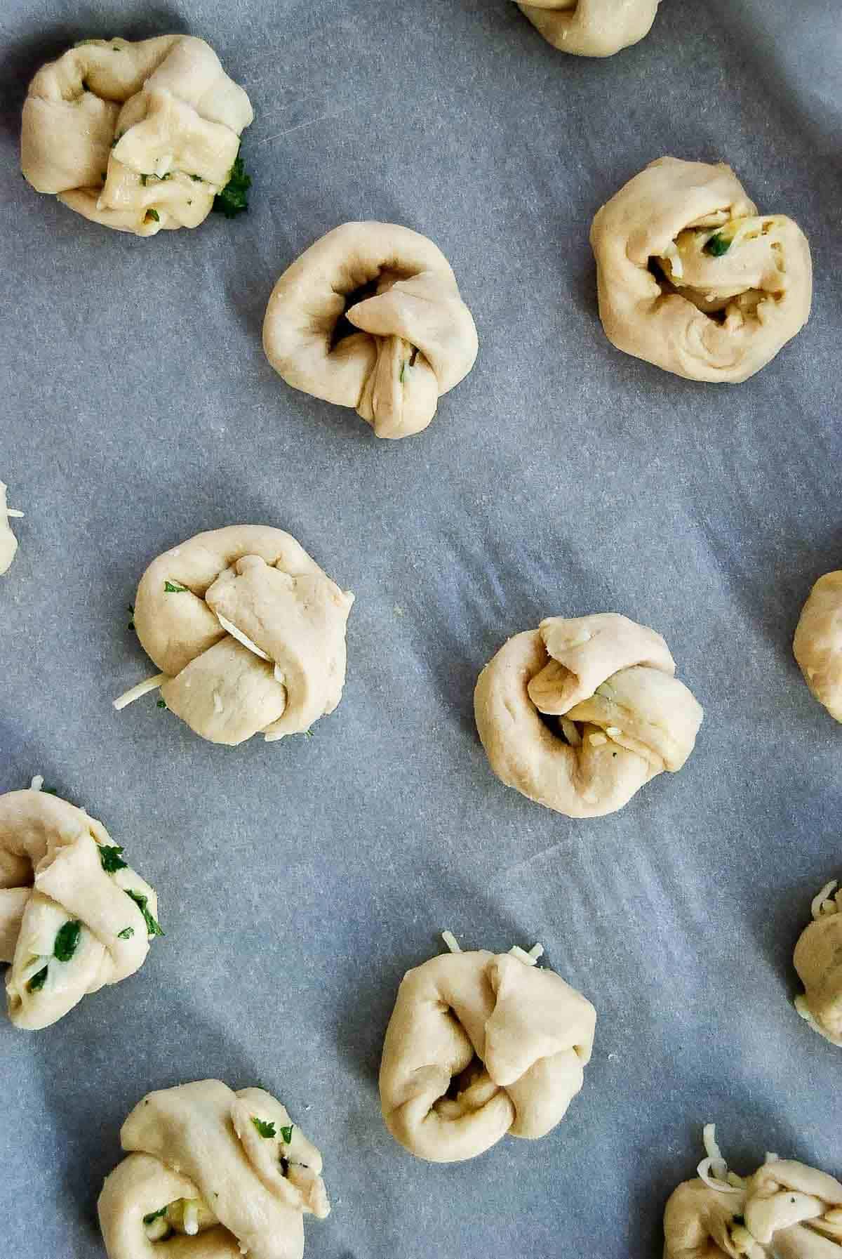 crescent roll dough rolled into garlic knots on baking sheet.