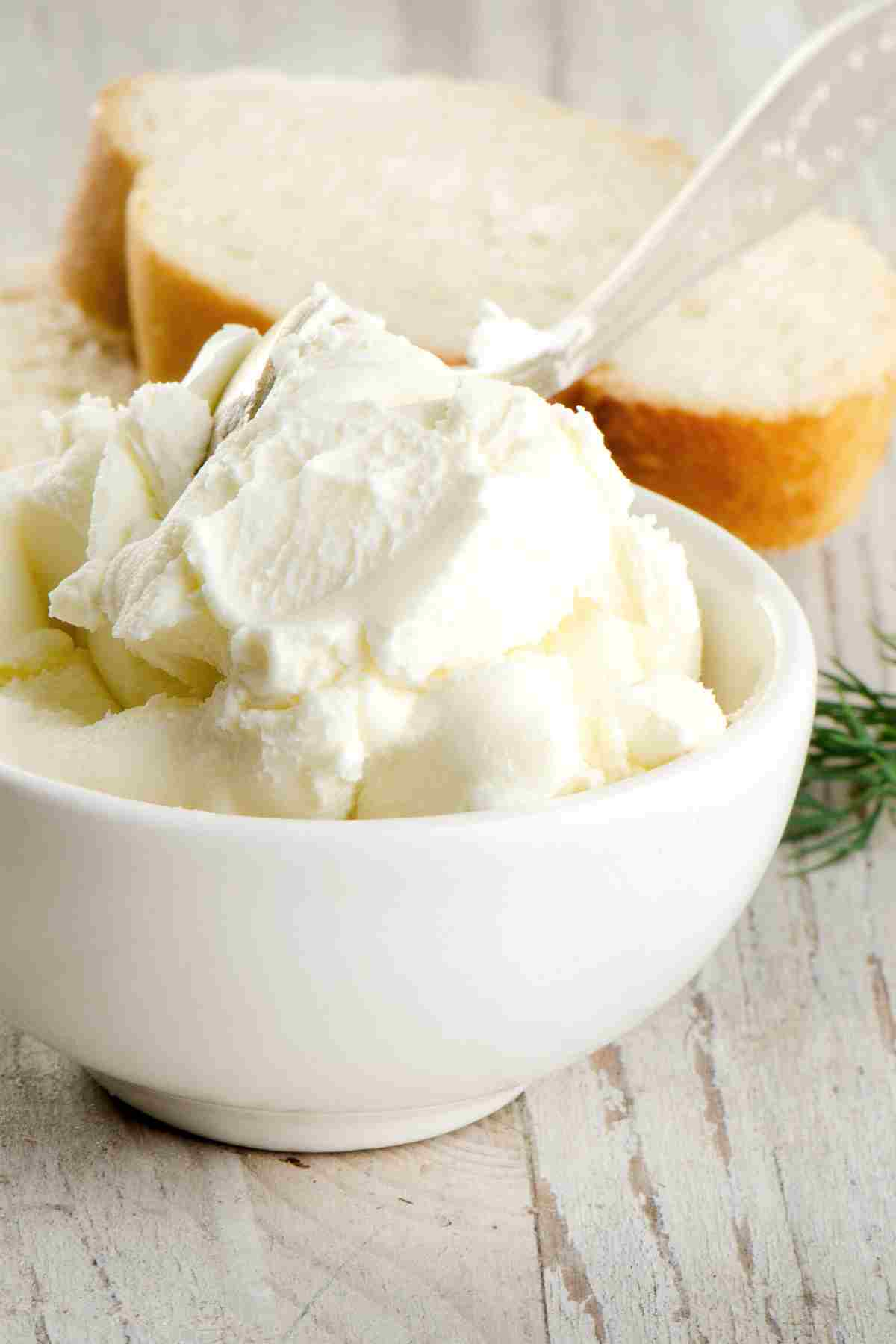 cream cheese in bowl next to slices of bread.