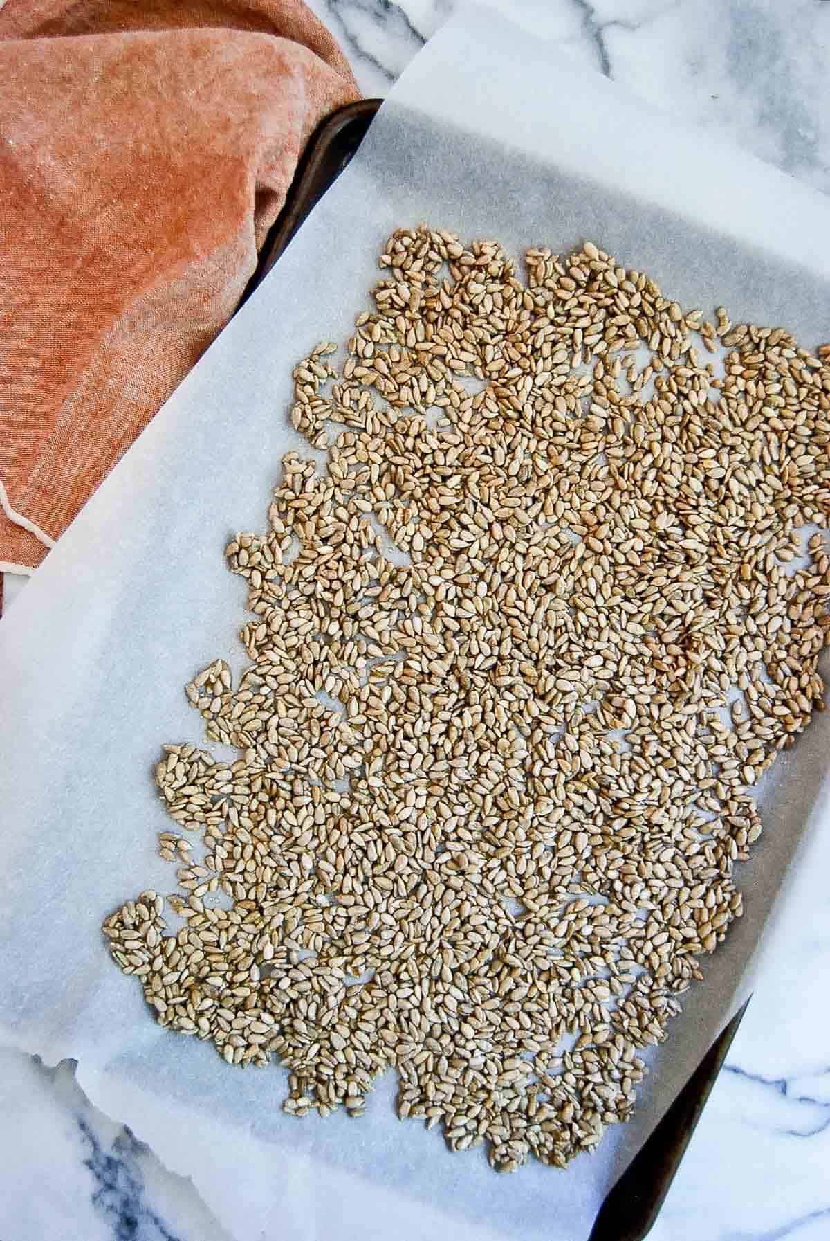 honey coated sunflower seeds spread evenly on baking sheet and parchment paper.