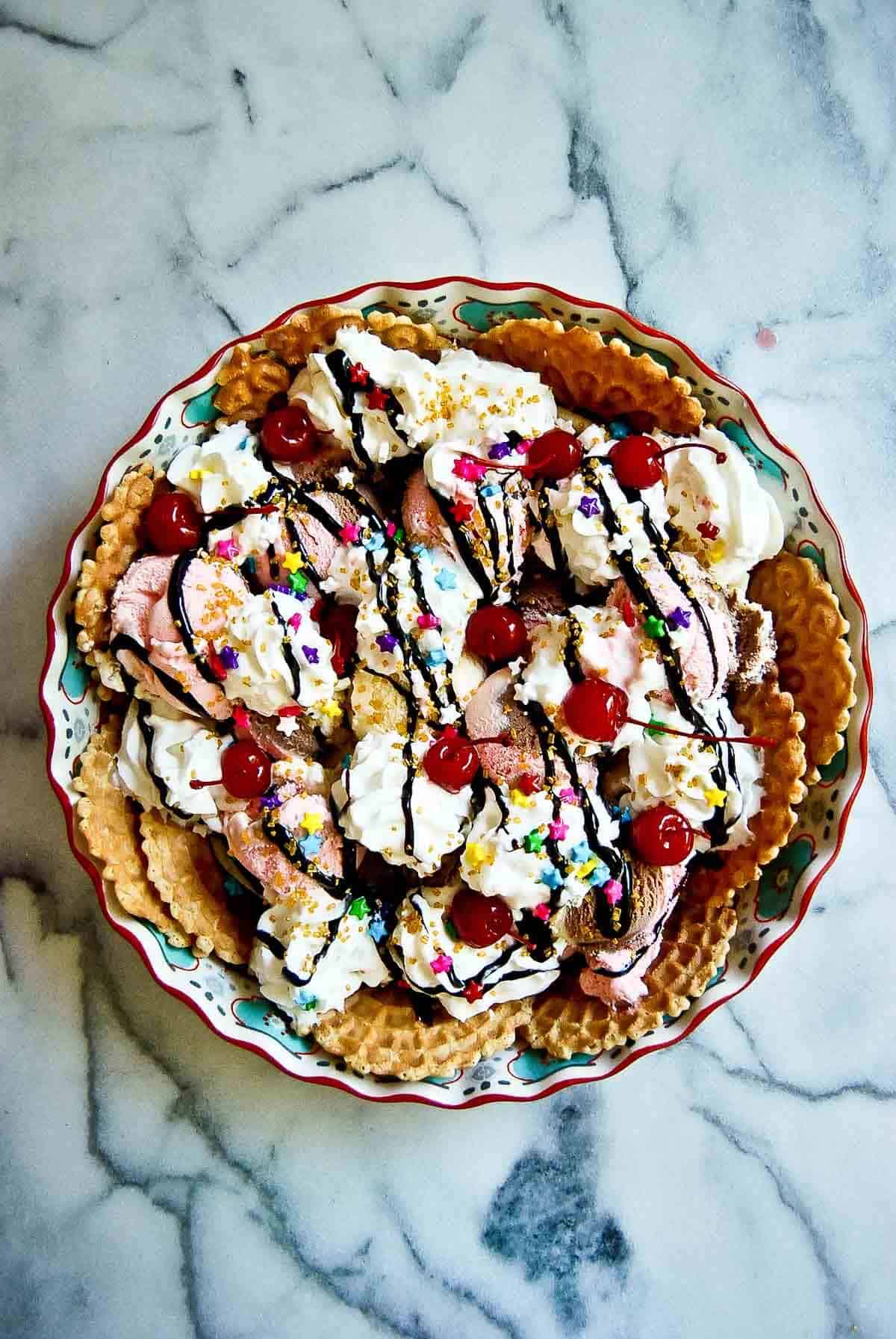 ice cream nachos with sprinkles, chocolate syrup, Marashcino cherries and whipped cream on counter top.