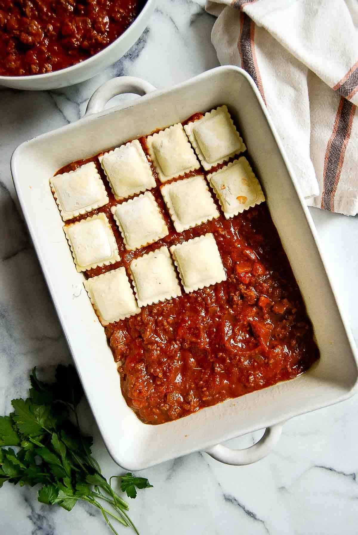 casserole dish with pasta sauce and frozen cheese ravioli being layered onto the top.