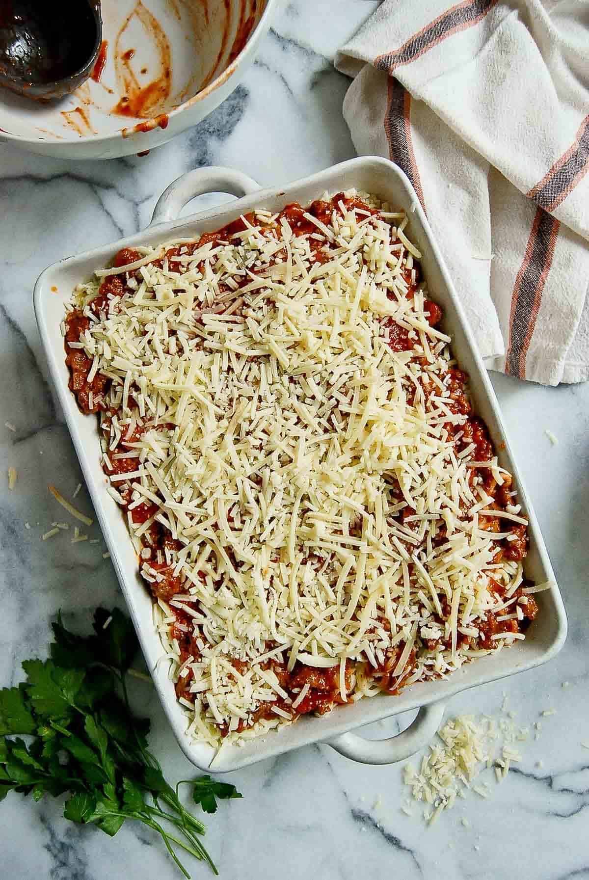 assembled lazy lasagna with layers of pasta, frozen cheese ravioli, and cheese in casserole dish.