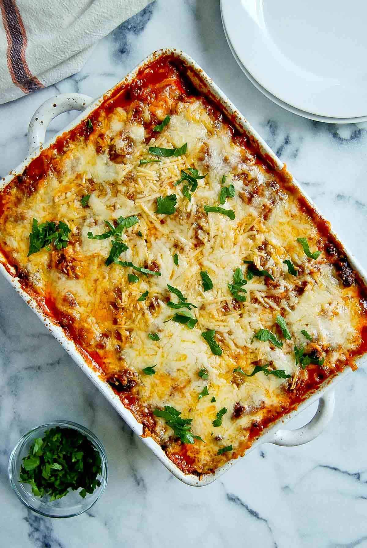 baked ravioli lasagna in casserole dish on cutting board.
