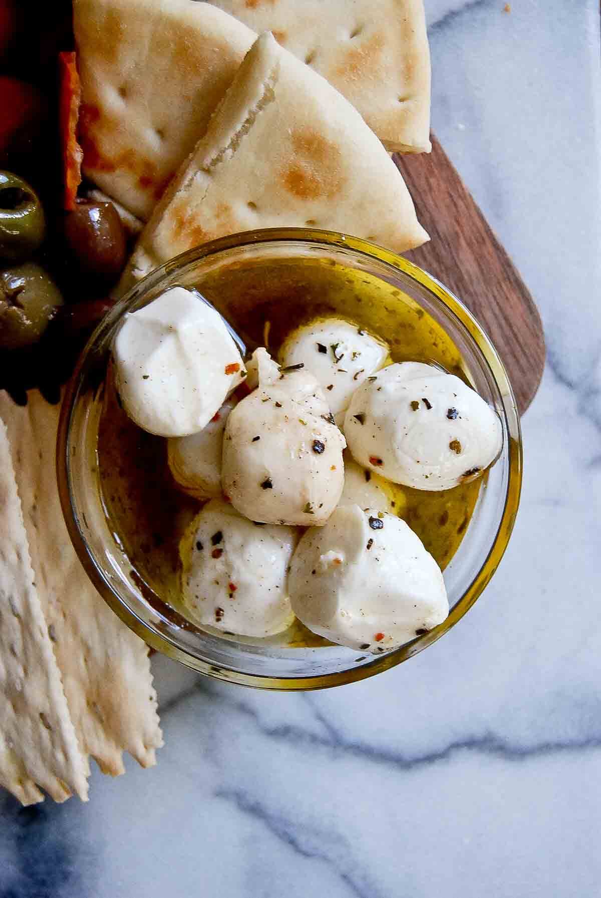 closeup of marinated mozzarella balls in olive oil and herbs on charcuterie board.