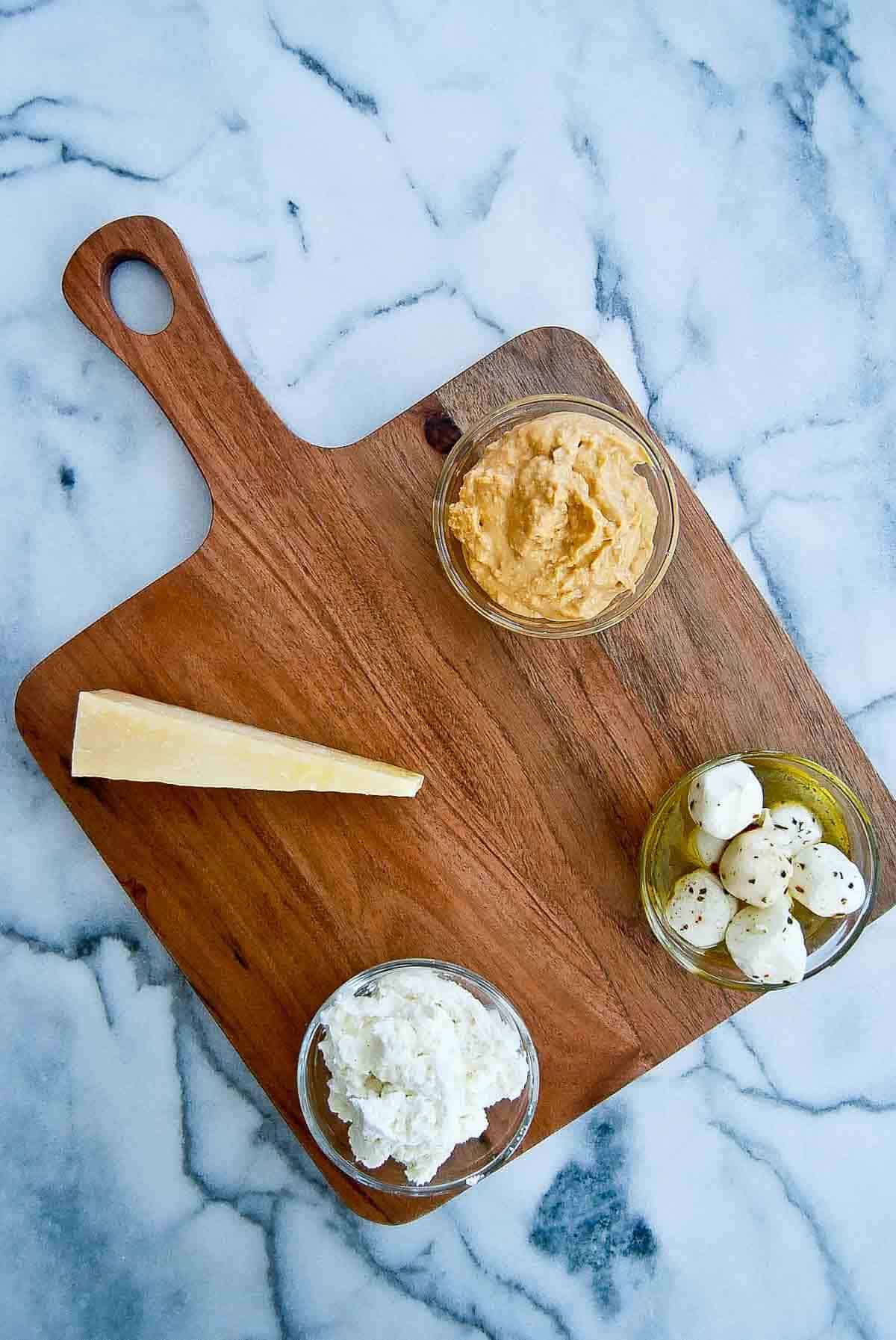 cutting board with cheeses hummus and dips.