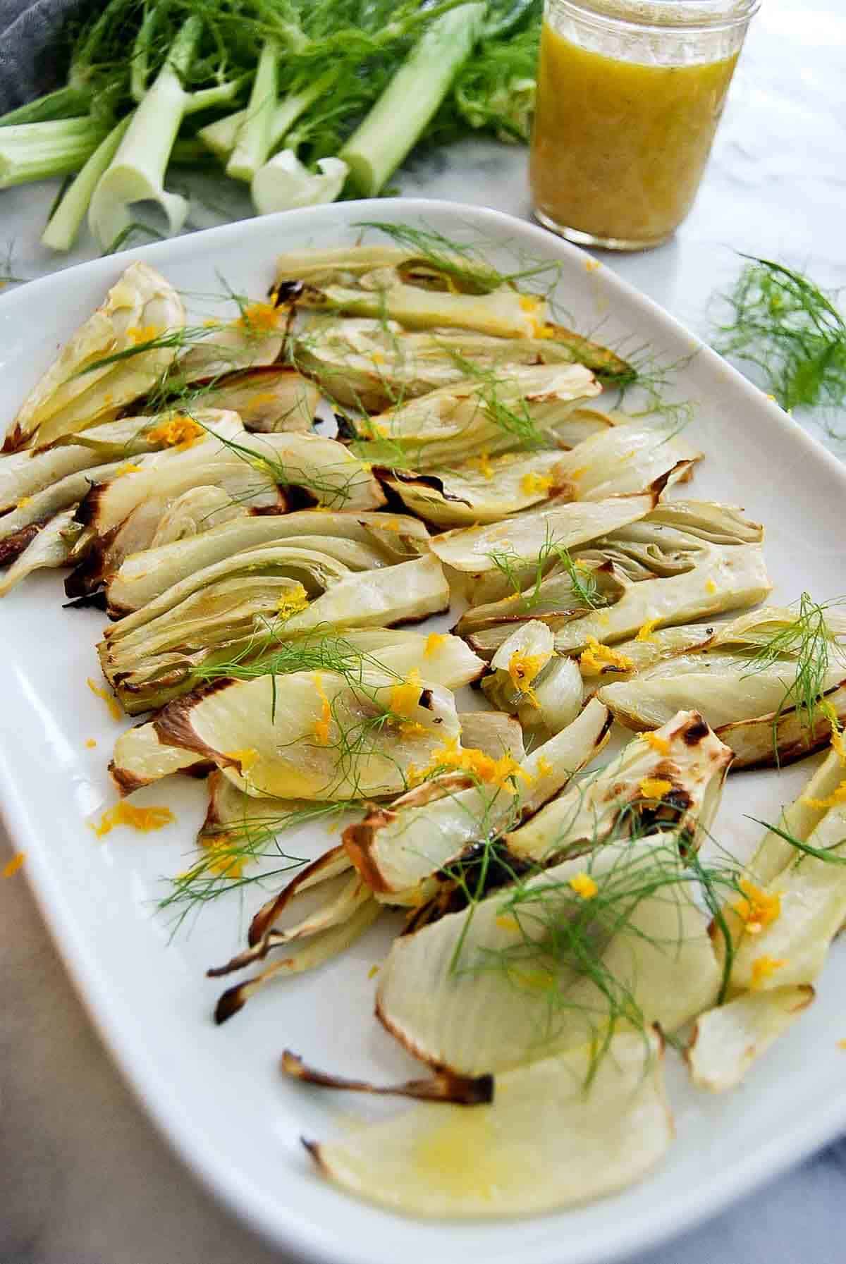 roasted fennel with orange honey dressing, fennel fronds, and orange zest on serving platter.