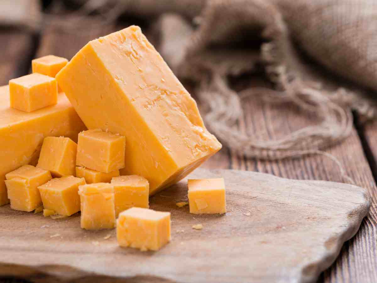 block of cheddar cheese on cutting board.