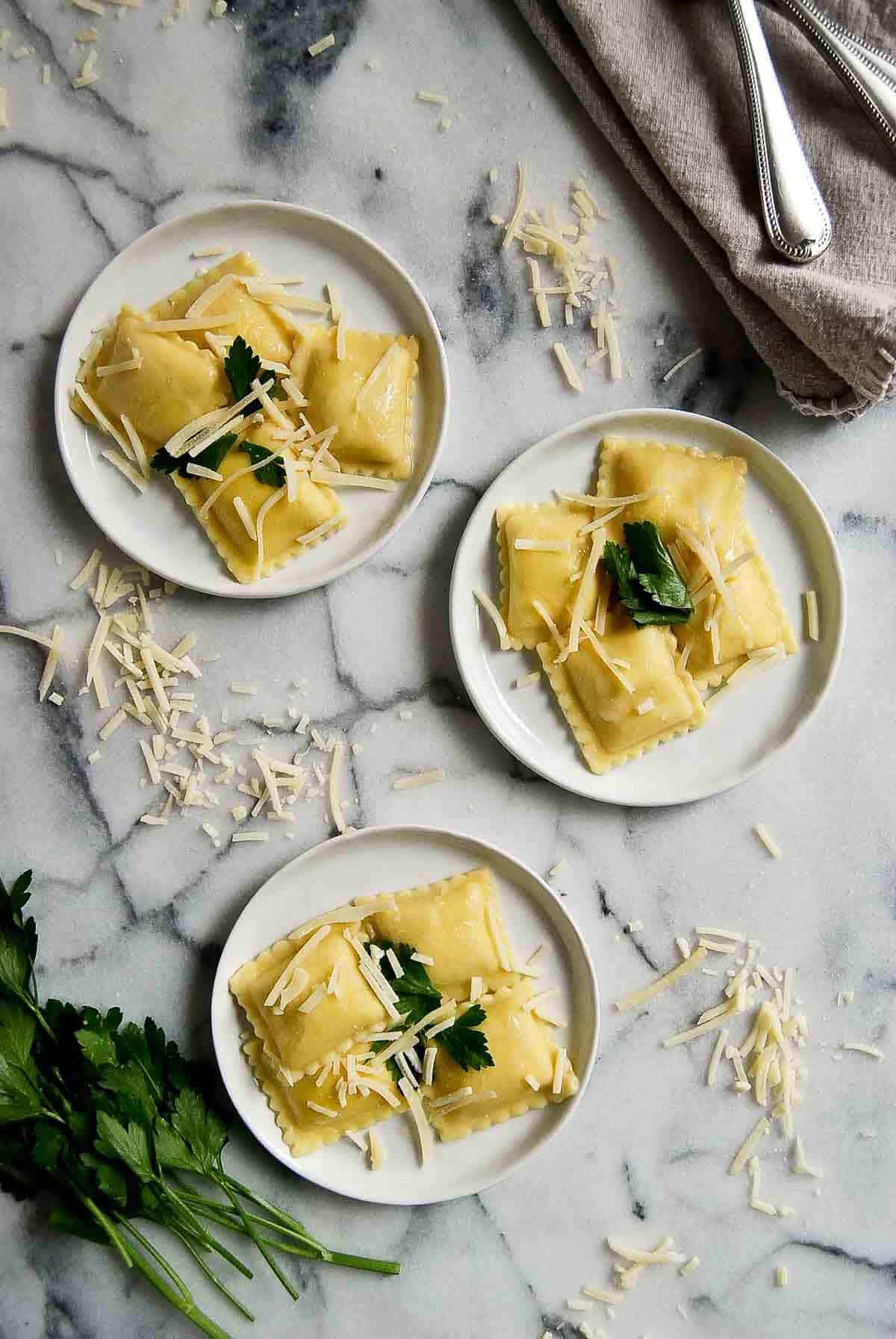 3 plates of cheese ravioli with garlic butter sauce, parmesan cheese and parsley.