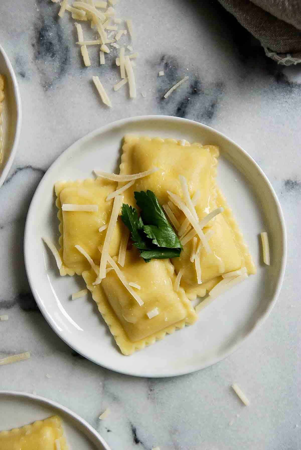 plate of cheese ravioli with garlic butter sauce, parmesan cheese and parsley. Cooking Frozen Cheese Ravioli is so easy and there are so many different ways you can use it! Below are my five favorite ways to cook frozen cheese ravioli for an easy meal or appetizer. Intro Frozen cheese ravioli is one of those freezer staples that I think everyone should have. It provides you with a simple way to make an endless variety of meals. Not only does it cook in minutes, but it’s incredibly versatile and can be used in so many ways to create a delicious dinner or appetizer. I’ve used it on its own in a simple pasta sauce, breaded baked to use as an appetizer with some marinara dipping sauce, or even as an easy substitute for noodles and ricotta cheese in a Lazy Lasagna. The options are endless and if you’re a parent, or simply a last-minute kind of cook (I happen to be both), frozen cheese ravioli is something you’ll want to have on hand almost all of the time. (You’ll always find a package of it in my freezer!). Why Use Frozen Ravioli? There are so many reasons this easy pasta has become a staple in our house: Cooks Fast. Sure, you can buy premade fresh ravioli, which probably tastes better, but if it’s speed you’re after, you can't beat frozen. Especially when you’re boiling it, frozen cheese ravioli cooks in less than 5 minutes. You can even cook the ravioli in a premade simmering sauce and you have a quick meal on the table in no time. Easy. Not only is this fast, but it’s a really easy way to make ravioli. No rolling out dough, no making your own cheese mixture, just plop it in some boiling water and you’re done. Or, use it as a shortcut to making a Lazy Day Lasagna recipe. Add some garlic bread and a simple salad and dinner is done! Delicious. Again, maybe homemade ravioli does taste a little bit better, but frozen is not far off, and once you add a sauce or some breading, the difference is minimal. Ingredients Here’s everything you’ll need to make frozen ravioli: A large pot of water Salt (for flavor) Extra Virgin Olive Oil (to prevent the ravioli from sticking together if boiling, or for crisping it up when baking or making it in the air fryer) Your favorite pasta sauce Optional: Cheese, if you’re making a casserole or want more to add to the top of your pasta dish. Breadcrumbs, fresh herbs, and eggs, if you’re making a toasted ravioli. The 5 Best Ways To Cook Frozen Cheese Ravioli Okay, so hopefully I’ve sold you on why frozen ravioli is a must-have for easy dinners. But, what’s the best way to make it? And how do you know when it’s finished? There are a variety of different methods of cooking frozen ravioli. Here are 5 easy ways to make this classic Italian staple. Boiled This is probably the fastest and easiest way to cook frozen cheese ravioli. Simply bring a large pot of water to a rolling boil. Add a little bit of salt to the water for seasoning. Add some extra virgin olive oil to the water to prevent the ravioli from sticking together. Then, simply boil for about 4-6 minutes, or until the ravioli floats to the top of the pot. For al dente ravioli (which basically means a pasta that is firm to the bite), remove immediately. Otherwise, the ravioli can continue cooking and may become a bit mushy and easily breakable. Add your favorite pasta sauce and you’ve got a delicious dinner on the table with minimal effort - perfect for busy weeknights. (See the recipe below for a great take on this easy cooking method. Baked Baked ravioli, especially when crispy and toasted can serve as a delicious appetizer with a side of marinara sauce for dipping. To make it, simply boil the ravioli for about 3 minutes to allow them to soften a bit. Then, create a breading with breadcrumbs, parmesan cheese, and Italian seasoning in one bowl, and crack a couple of eggs in another. Dip the ravioli in the egg mixture, and then in the breadcrumbs mixture to coat. Then place the ravioli on a pan lined with parchment paper and bake until golden brown and crispy. In the air fryer You can make toasted ravioli in the air fryer too! Follow the instructions above for the breading, then arrange the ravioli in an even layer in your air fryer. Bake at 400 degrees for 3 minutes, then flip and bake for an additional 3-4 minutes until the breading is crispy. To make the ravioli in the air fryer without the breading, simply brush the ravioli with some oil, place it in the air fryer, and cook as directed above. The ravioli will come out crispy and delicious! In a lasagna Frozen cheese ravioli is such a great cooking hack when making this classic Italian dish and you can do it in just a few simple steps. Simply layer your favorite sauce at the bottom of a casserole dish, add the frozen ravioli directly on top of the sauce in a single layer, then add more sauce and Parmesan and mozzarella cheese. Repeat the layers and bake the dish in the oven and you’ll have a delicious ravioli casserole in about an hour. In the microwave Don’t want to mess with your stove or oven? Ravioli can easily be made in the microwave too. Simply add the ravioli to a microwave save bowl filled with salted water and a teaspoon of olive oil, cover with plastic wrap be sure to cut a slit in the middle to allow it to vent, and cook the ravioli on high for about 5-6 minutes, checking it periodically to see if the ravioli is floating or not (you’ll know it’s done if it floats!). Then add to a sauce and serve for a tasty meal! Variations As you can see, there are lots of ways to prepare frozen ravioli. But what about serving it? Below are some ways to add different flavors to your dish. Vary your sauce. Sure, a classic tomato-based spaghetti sauce is a popular choice, but changing up your sauce can totally change the flavor of your meal. Add some ground beef or ground turkey to the sauce, incorporate some fresh garlic, or choose something totally different from tomato sauce, like a pumpkin sauce or alfredo sauce. Add some fresh herbs or spices. A little bit of oregano, thyme, or even marjoram can really amp up the flavor of your ravioli. Add it to the sauce, or simply sprinkle it a top of a simple butter sauce for some extra flavor. Even simply adding a bit of crushed red pepper flakes, garlic powder, or a grind of black pepper can add some good flavor to your delicious meal. Vary the cheese. Parmesan cheese and mozzarella are two obvious choices when you’re choosing cheese, but you could also choose something like goat cheese to add a more creamy texture, or blue cheese or gorgonzola for a little more punch. Choose a different type of ravioli. I find cheese ravioli to be the most versatile type of ravioli to keep on hand, but you can easily find different variations at your local grocery store. Look for meat-based ravioli, butternut squash, or even spinach for some different options. ​Helpful tips No matter what your cooking method, there are a few things to remember if you want perfect ravioli. Consider the steps below for the best results: 1. Don't crowd the ravioli. If you're boiling your ravioli, make sure to use enough water so that the ravioli has room to spread out a bit. Otherwise, the ravioli may stick together when cooking. If baking or air frying, be sure to spread out in a single layer to ensure everything cooks evenly and the ravioli are allowed to get a bit crispy. ​2. Use olive oil. When boiling, the olive oil can help prevent the ravioli from sticking together. And if baking or air frying, it can create a crispy exterior that's great for appetizers or for making a toasted ravioli recipe. FAQ How long does cooking frozen ravioli take? The cooking time will vary by the method you use. Frozen ravioli will boil in about 4-6 minutes. If you're making the ravioli in the air fryer, you'll need about 7 minutes, and if baking, you'll need roughly 10 minutes. Can you cook frozen ravioli without thawing? Yes! Frozen ravioli cooks easily without thawing which makes it a great way to make an easy meal quickly. It also makes it a good staple to keep on hand in your freezer. How long should you boil frozen ravioli? As a general rule, frozen ravioli takes about 4-6 minutes to boil. But it's also a good idea to check your package instructions to make sure since different brands or types of ravioli may require a shorter or longer cook time. How can you tell ravioli are done cooking? You'll know the ravioli cooked through when they float to the top of the pan when boiling. How do you cook frozen ravioli without breaking them? One common complaint with boiling ravioli is that they're easy to break. This often is a result of cooking the ravioli for too long, which can make it mushy. Don't let your ravioli sit in boiling water for too long to avoid this. Can you cook frozen ravioli in the air fryer? Yes! Cooking frozen ravioli in the air fryer is a delicious way to make toasted ravioli. Simply brush with oil, then air fry at 400 degrees F for about 7 minutes, flipping the ravioli halfway through. You can also add a breading to the ravioli for some extra flavor. Mix bread crumbs, Italian seasoning, and parmesan cheese in a small bowl, and crack three eggs in a second bowl. Dip the ravioli in the egg mixture, then again in the breadcrumb mixture, and then cook as directed above for a tasty appetizer. Can you bake frozen ravioli instead of boiling? Sure can! Boil the ravioli for about three minutes to soften them, then brush oil and arrange them in an even layer on a baking dish or tray and bake for about 10 minutes at 400 degrees F. For toasted ravioli, mix bread crumbs, Italian seasoning, and Parmesan cheese in a small bowl, and crack three eggs in a second bowl. Dip the ravioli in the egg mixture, then again in the breadcrumb mixture, and then cook as directed above. Can you cook frozen ravioli in the microwave? Yes! Add the ravioli to a microwave-safe bowl filled with water (be careful not to crowd the ravioli!). Cover with vented plastic wrap and cook on high for about 7 minutes, or until the ravioli floats in the water. How to prevent ravioli from sticking together when cooking? A great way to prevent sticking when boiling ravioli is to add a small drop of olive oil to the water. This makes it easy for the ravioli to be separated if they happen to stick together slightly. How do I store cooked ravioli? If you find yourself with leftover cooked ravioli, simply allow it to cool completely, then store it in an airtight container in the refrigerator. Cooked ravioli will keep for about 4-5 days when stored in the fridge. Easy Recipe For Frozen Cheese Ravioli 1 lb cheese ravioli ½ teaspoon salt 1 tablespoon extra virgin olive oil 3 tablespoon melted butter or extra virgin olive oil 4 garlic cloves, minced ¼ cup parsley, chopped ¼ cup shredded parmesan Fill a large pot with water. Add the salt and 1 tablespoon of olive oil and bring to a boil. Add the ravioli to the large pot of salted water and continue boiling until the ravioli float to the top. Carefully remove the ravioli with a slotted spoon and place it onto a tray lined with a paper towel, or in a colander. While the ravioli is cooking, prepare the garlic butter. Melt 3 tablespoon of butter in a small saucepan over medium heat. Add the minced garlic and saute for 1-2 minutes, or until the garlic is fragrant and softened. Pour the garlic sauce over the cooked cheese ravioli and toss gently to combine, being careful not to break the ravioli pieces. Serve in individual bowls or plates and top with parsley and parmesan.