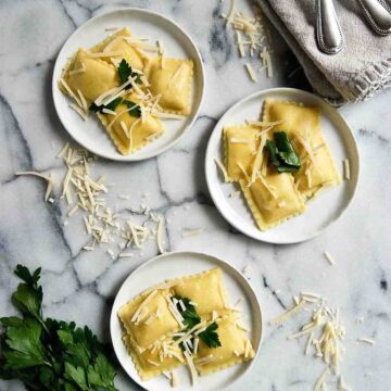 3 plates of cheese ravioli with garlic butter sauce, parmesan cheese and parsley.