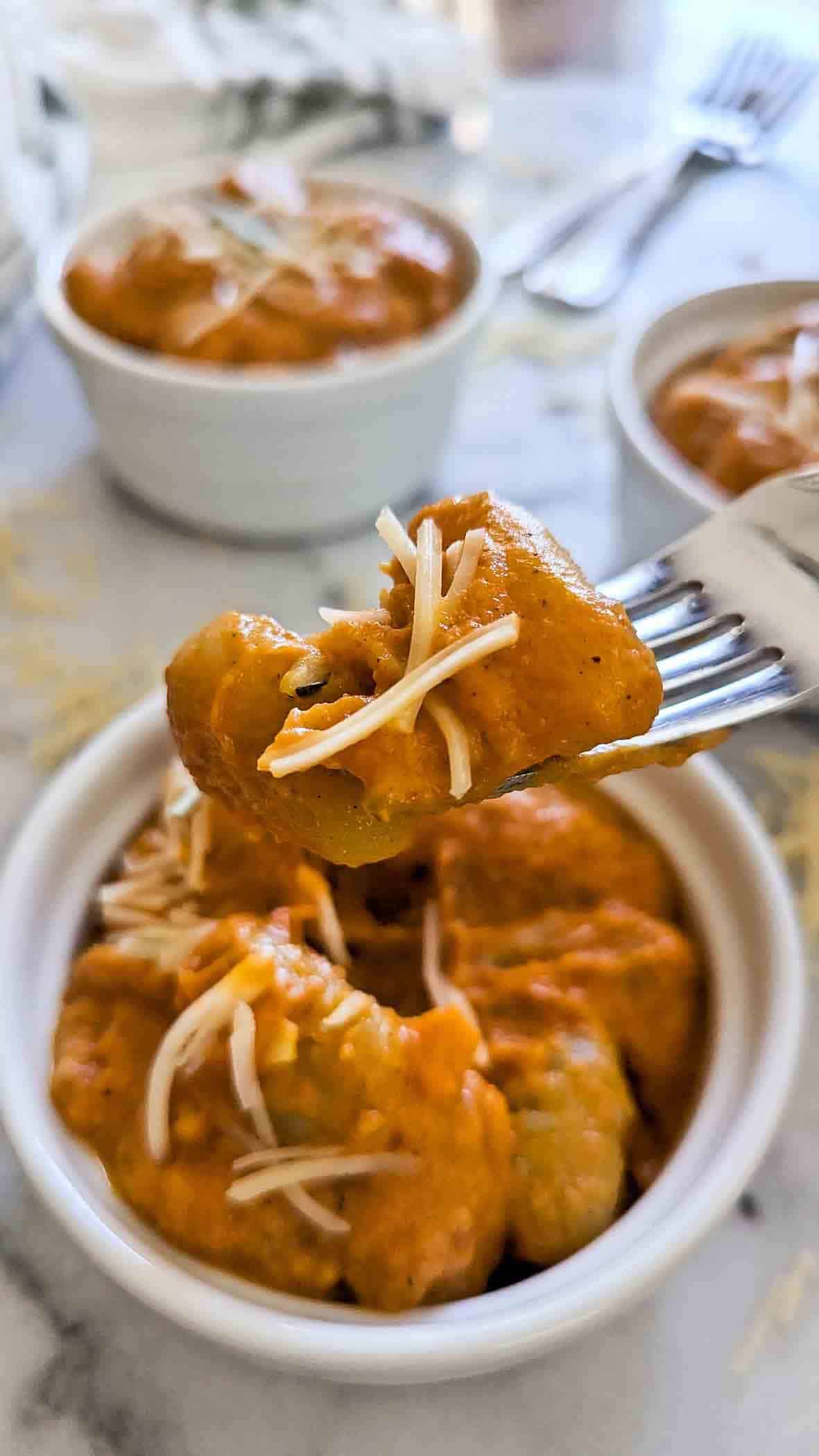 gnocchi with pumpkin sauce on fork with bowls in the background.