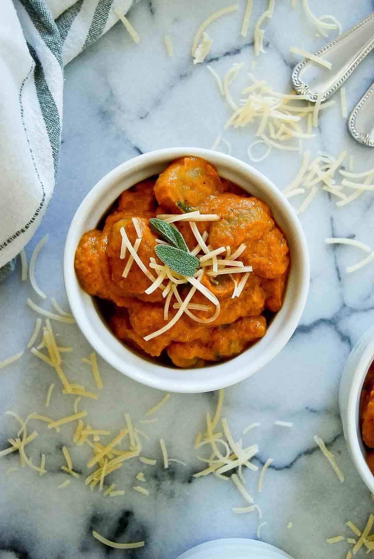 closeup of pumpkin gnocchi sauce in bowl with parmesan and sage.