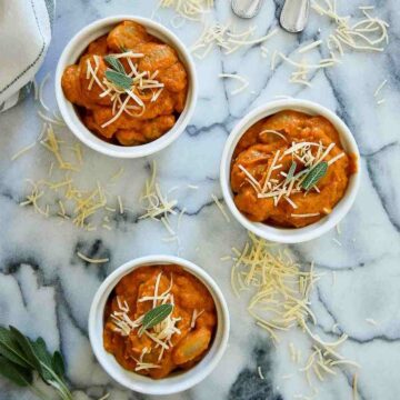 three bowls of pumpkin gnocchi sauce in bowls with parmesan and sage on top.