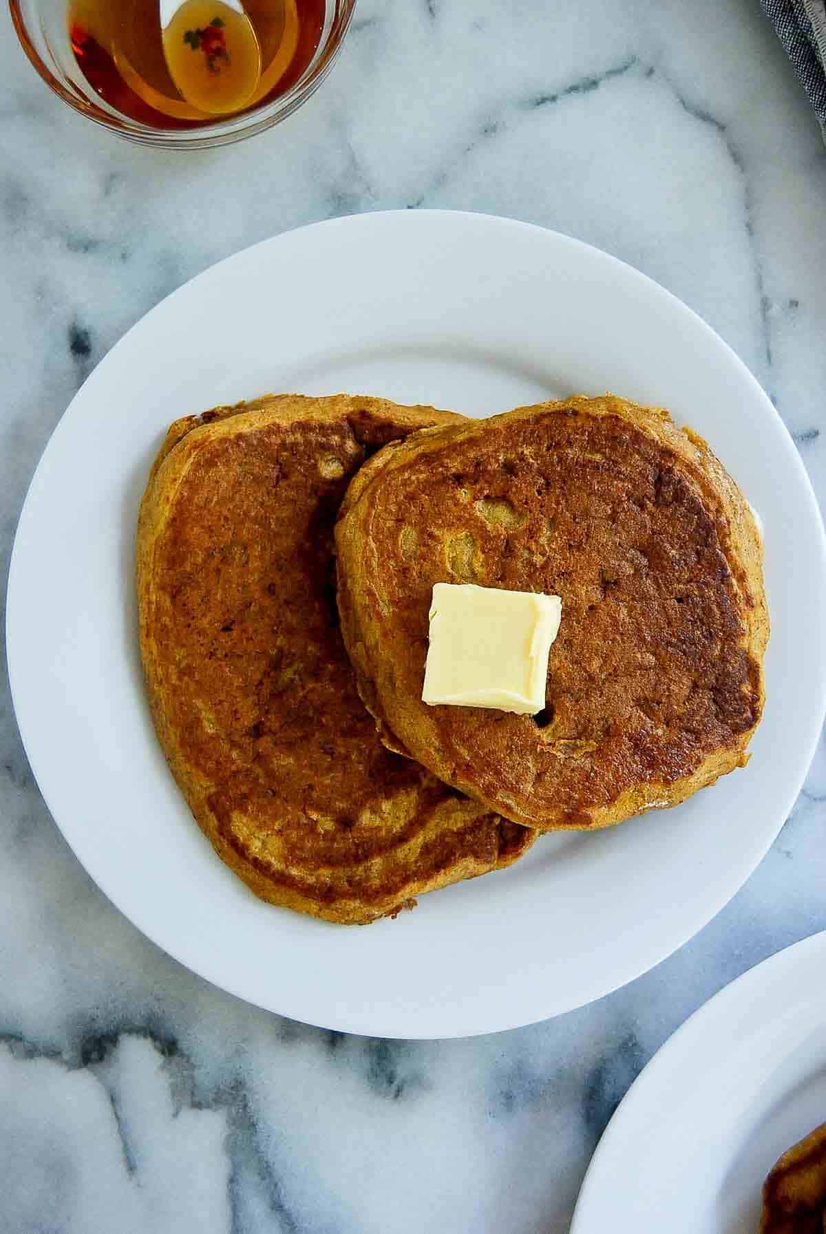 two pumpkin pancakes on plate with butter tab.