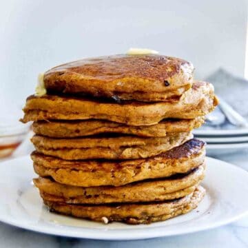 side view of pumpkin pancakes, stacked on plate with butter dripping down the side.
