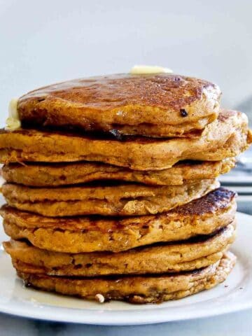 side view of pumpkin pancakes, stacked on plate with butter dripping down the side.