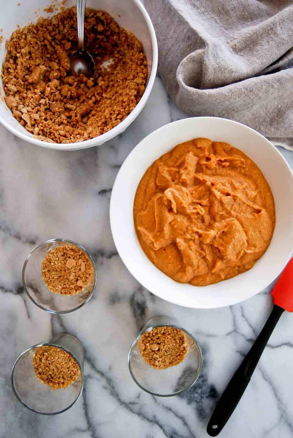 graham cracker crumbles added to small cups on countertop.