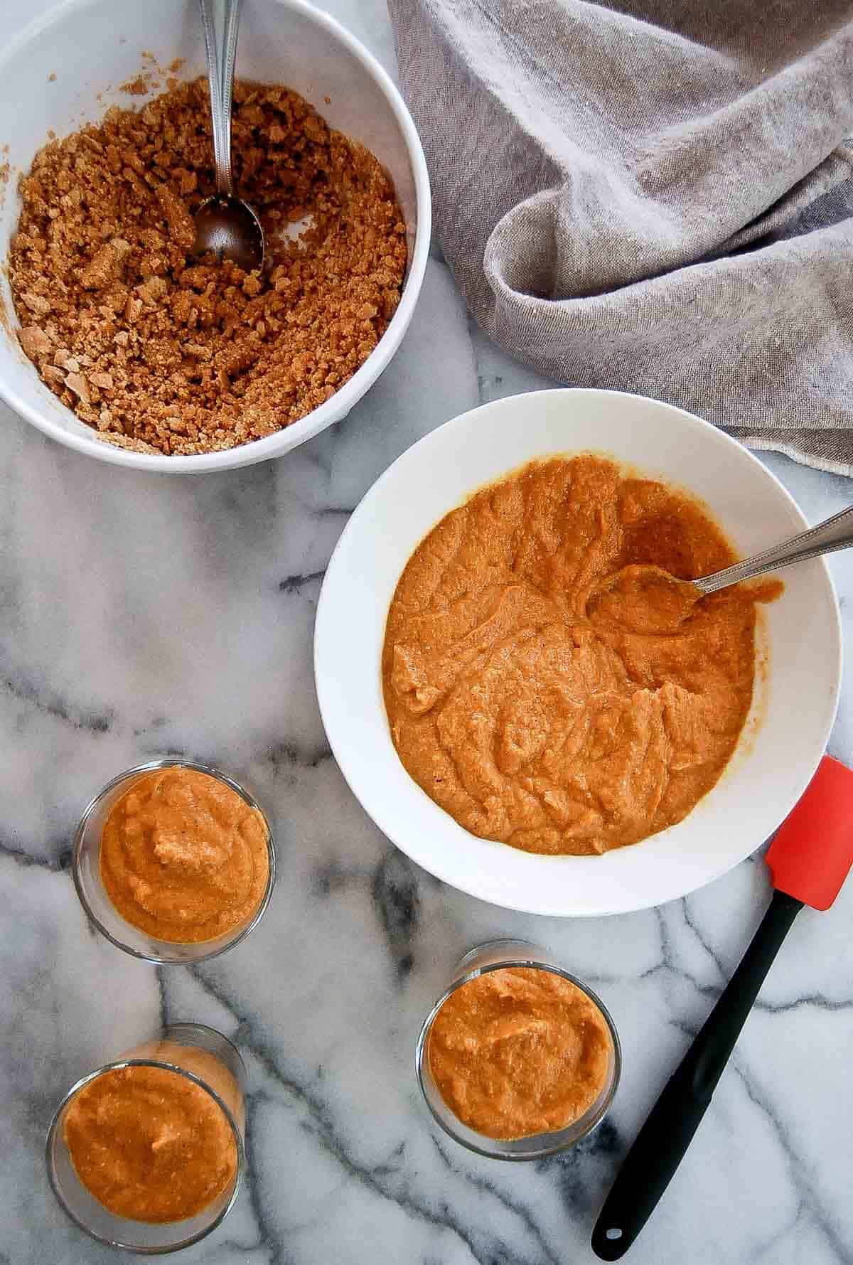 pumpkin pie filling added to the top of graham cracker crust in three small cups on countertop.