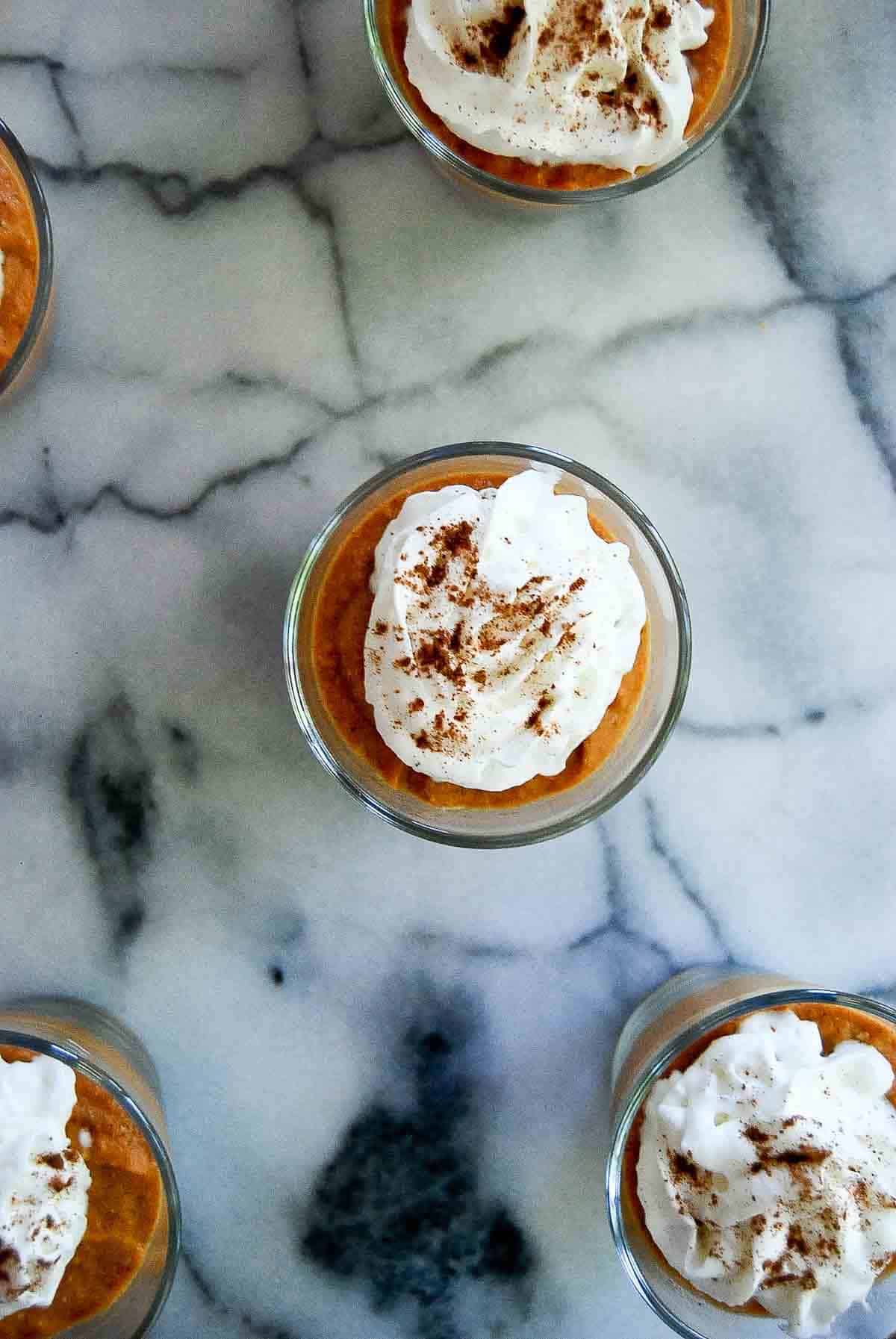 top down view of pumpkin pie in a cup topped with whipped cream and cinnamon.